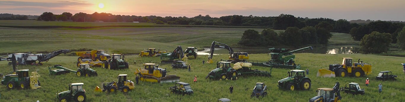 Menschen, die zwischen unterschiedlichen Arten von Ausrüstung von John Deere auf einem großen Feld umhergehen