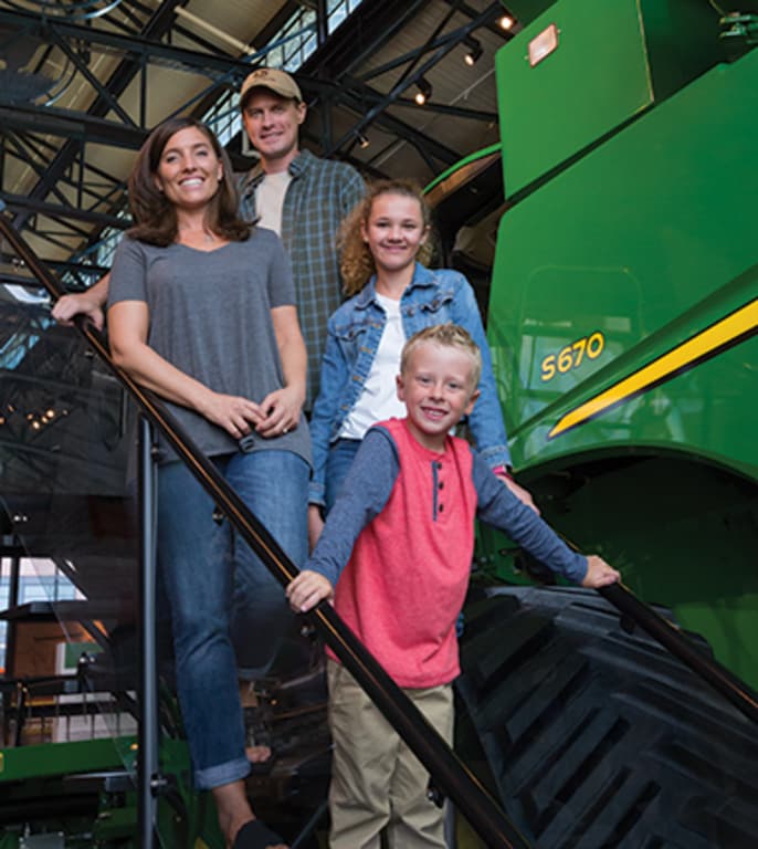 A family of four poses in front of a combine at the John Deere Pavilion