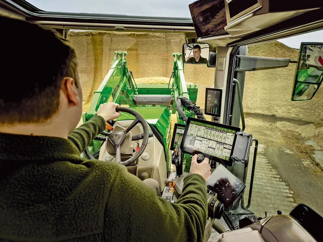 Vue de l’intérieur de la cabine d’un tracteur John Deere montrant les commandes de l’utilisateur et le fonctionnement du chargeur frontal.
