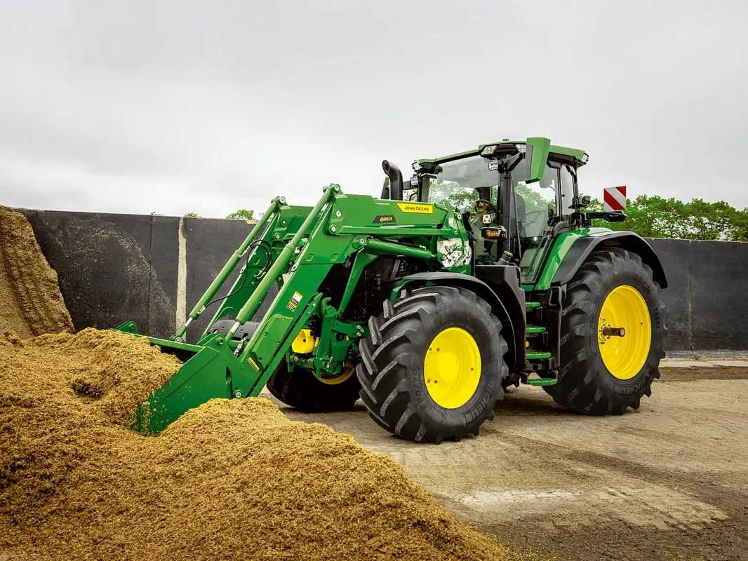 Tracteur John Deere en train de pousser un tas d’ensilage à l’aide du godet de son chargeur frontal, dans un environnement agricole.