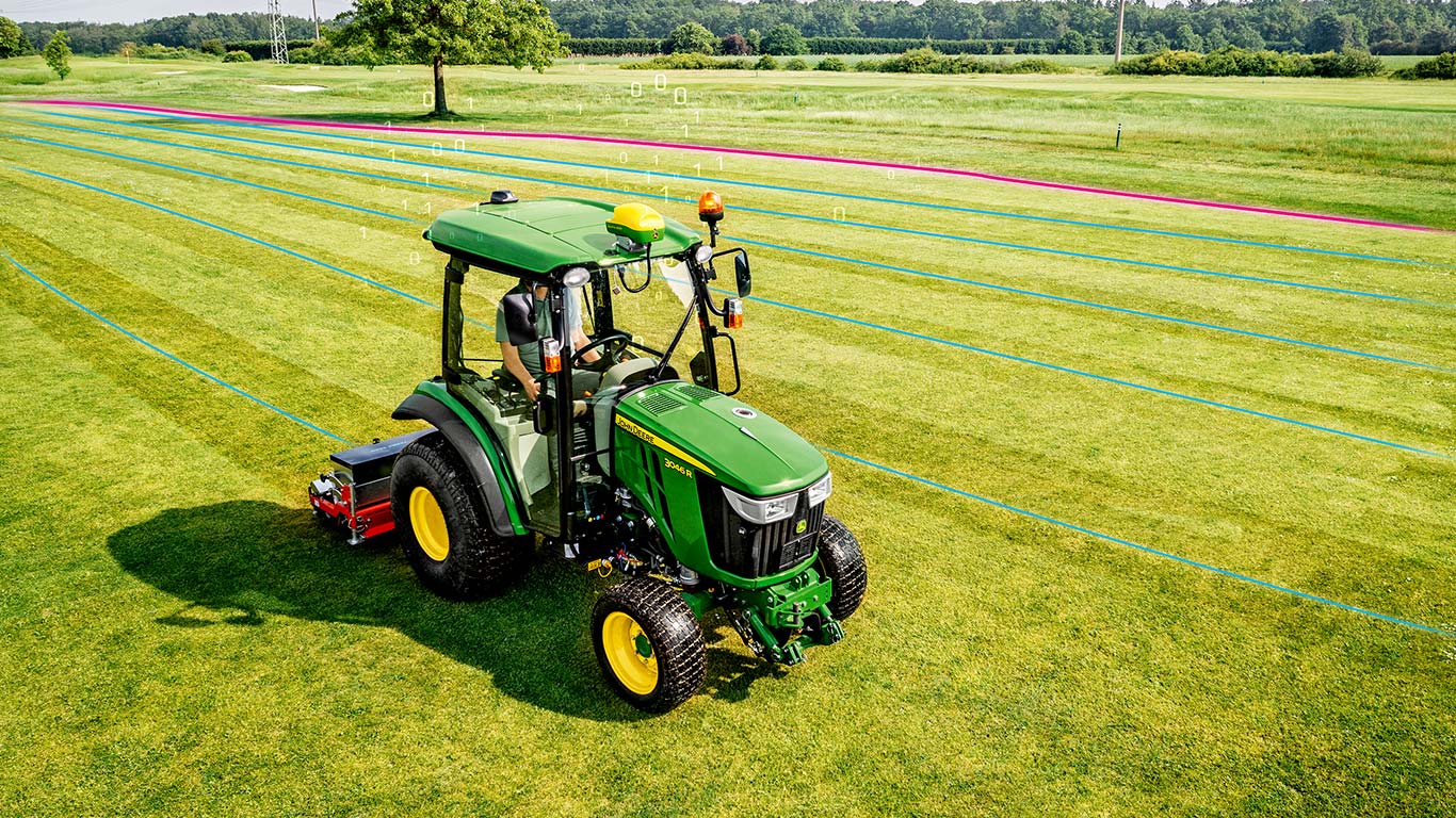 Ein Greenkeeper arbeitet auf einer Rasenfläche mit einem Kompakttraktor von John Deere.