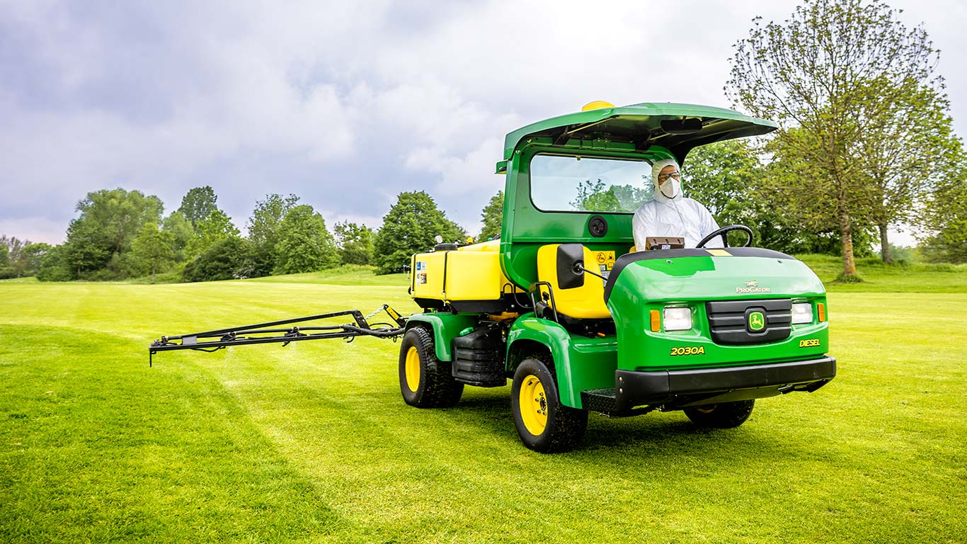 Ein Greenkeeper in Schutzkleidung arbeitet auf dem Rasen eines Golfplatzes mit einer John Deere Feldspritze.