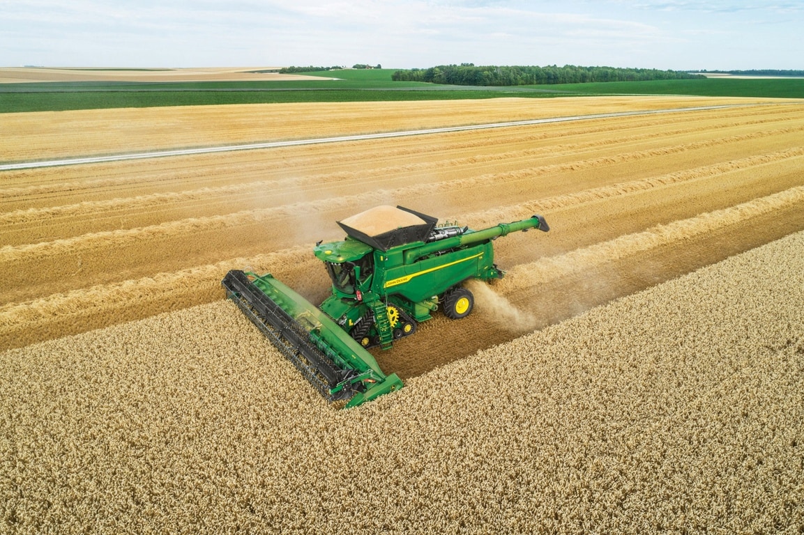 Vue aérienne d’une moissonneuse-batteuse récoltant du blé sur fond de plusieurs champs, illustrant les modes d’exploitation agricole à grande echelle