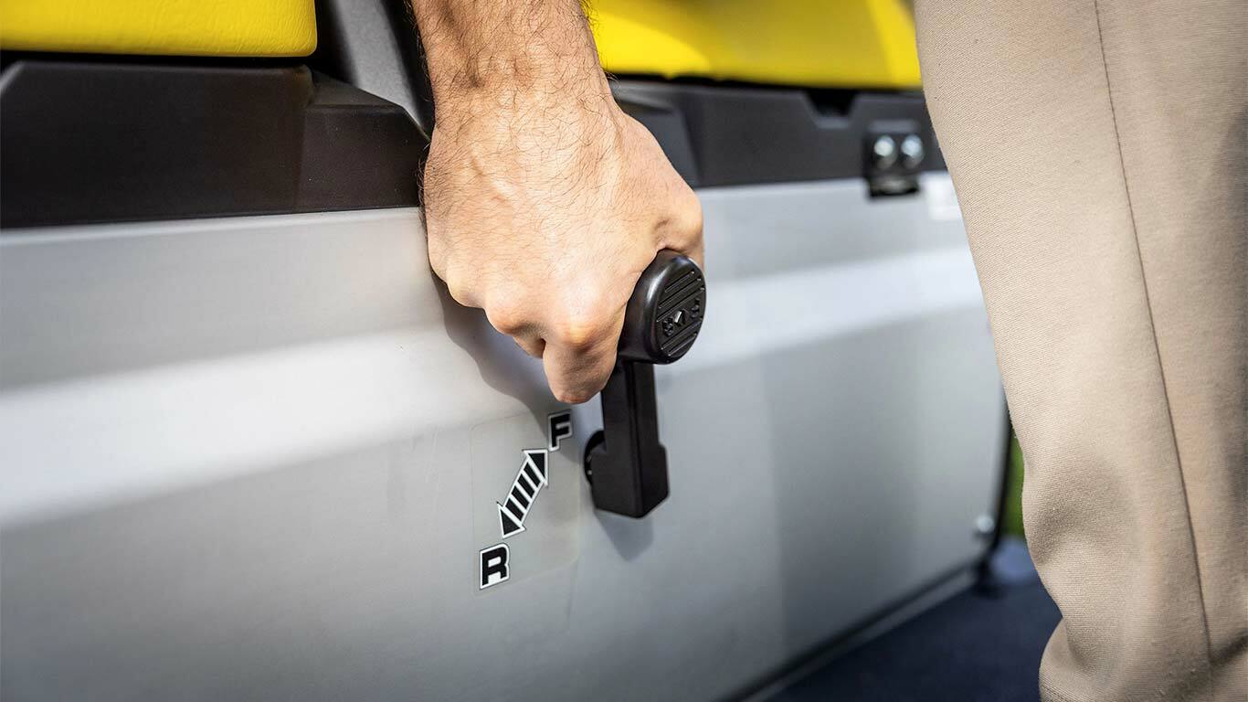 Gros plan d’une main actionnant le levier de vitesses d’un Gator&nbsp;GS John&nbsp;Deere pour montrer les rapports avant et arrière à côté des sièges jaunes.