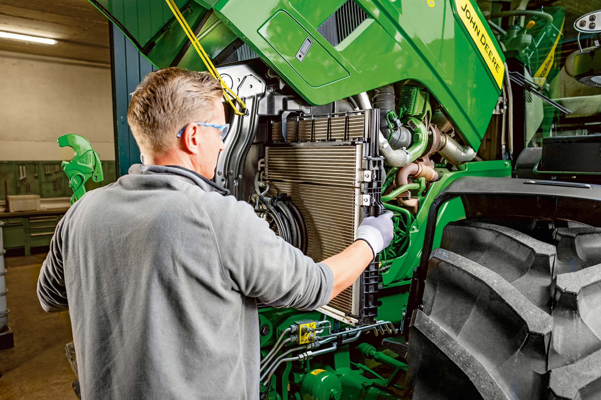 Un technicien effectuant des travaux d’entretien dans le compartiment moteur d’un tracteur John&nbsp;Deere de la série&nbsp;6M.