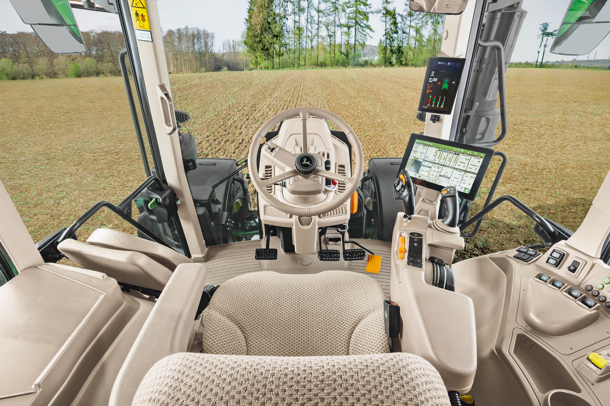 Vue d’ensemble de l’intérieur de la cabine d’un tracteur John Deere de série 6M, avec le siège du conducteur, le volant et les consoles numériques.