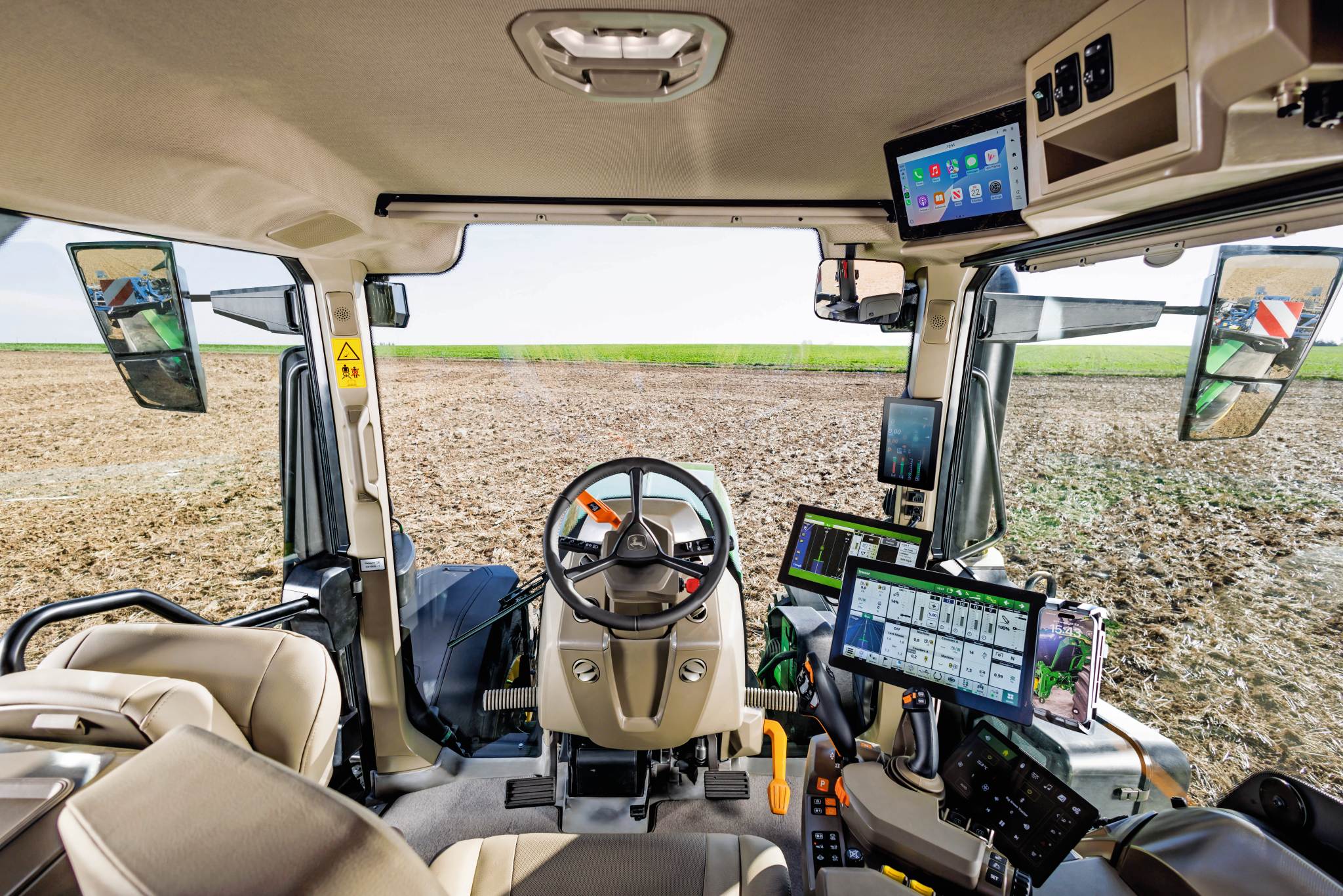 Intérieur d’une cabine de tracteur moderne, avec volant, consoles tactiles et commandes d’agriculture de précision, donnant sur un champ cultivé